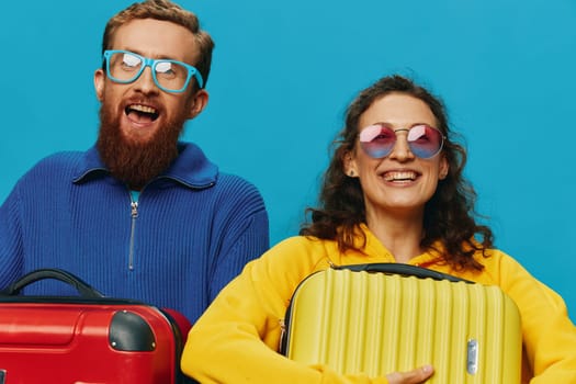 Woman and man smile suitcases in hand with yellow and red suitcase smile fun, on blue background, packing for a trip, family vacation trip. High quality photo