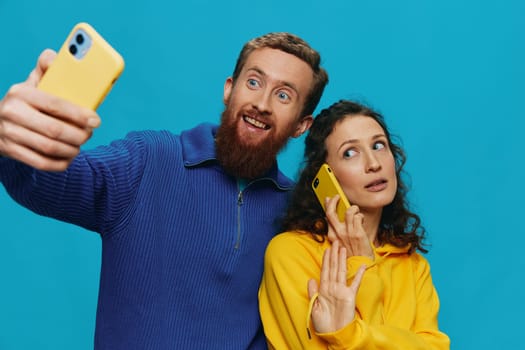 Woman and man funny couple with phones in hand taking selfies crooked smile fun, on blue background. The concept of real family relationships, talking on the phone, work online. High quality photo