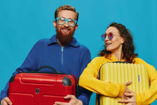 Woman and man smile suitcases in hand with yellow and red suitcase smile fun, on blue background, packing for a trip, family vacation trip. High quality photo