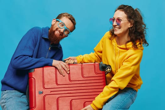 Woman and man smile suitcases in hand with yellow and red suitcase smile fun, on blue background, packing for a trip, family vacation trip. High quality photo