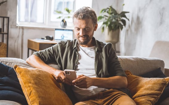 Man sitting at home office desk, focused on mobile phone. Concept of remote work and freelance, as man using smartphone to stay connected and productive while working from home. High quality photo