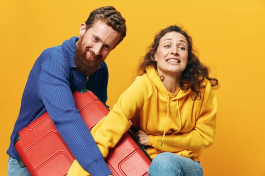 Woman and man smiling, suitcases in hand with yellow and red suitcase smiling merrily and crooked, yellow background, going on a trip, family vacation trip, newlyweds. High quality photo