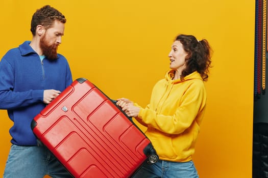 Woman and man smiling, suitcases in hand with yellow and red suitcase smiling merrily and crooked, yellow background, going on a trip, family vacation trip, newlyweds. High quality photo