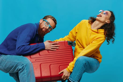 Woman and man smile suitcases in hand with yellow and red suitcase smile fun, on blue background, packing for a trip, family vacation trip. High quality photo