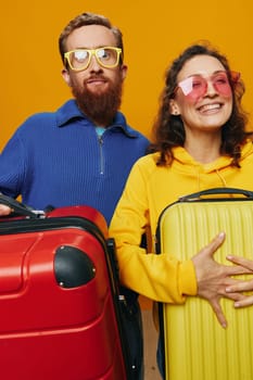 Woman and man smiling, suitcases in hand with yellow and red suitcase smiling merrily and crooked, yellow background, going on a trip, family vacation trip, newlyweds. High quality photo