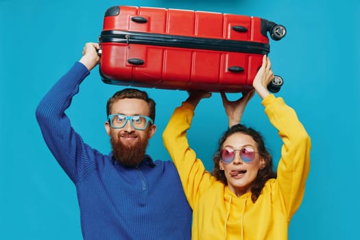 Woman and man smile suitcases in hand with yellow and red suitcase smile fun, on blue background, packing for a trip, family vacation trip. High quality photo