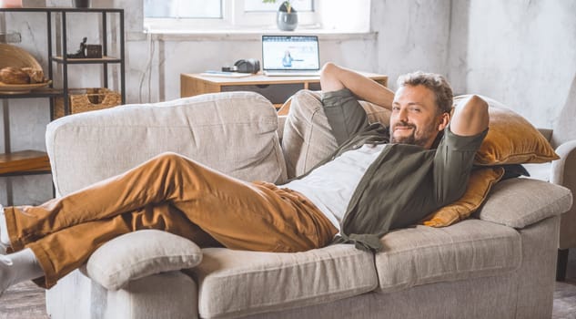 Man enjoying peaceful moment home, laying comfortably on sofa. Concept of freelancing and working from home, which has become increasingly popular in recent years. Handsome spent time home. High quality photo