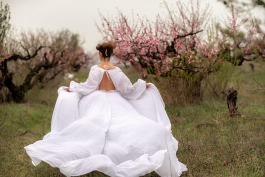 Woman peach blossom. Happy curly woman in white dress walking in the garden of blossoming peach trees in spring.