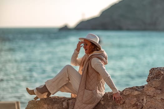 Happy blonde woman in a white suit and hat posing at the camera against the backdrop of the sea.