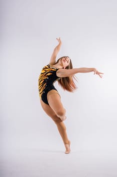 A girl gymnast in a swimsuit does tricks on white and dark background. Front view