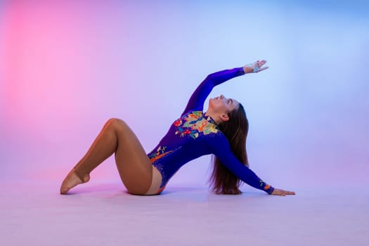 A girl gymnast in a swimsuit does tricks on white and dark background. Front view