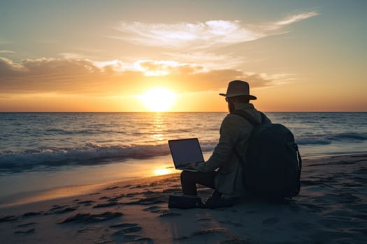 Young man with backpack using laptop computer on a beach at sunset. Freelance work concept