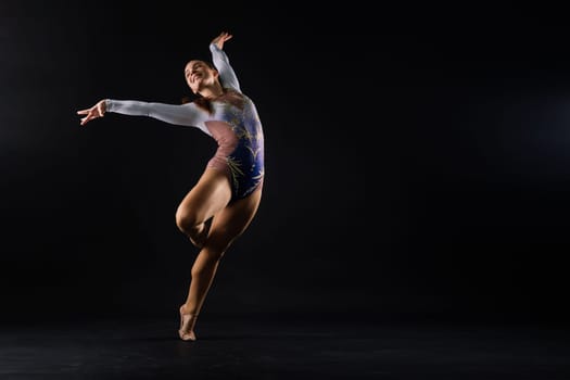 A girl gymnast in a swimsuit does tricks on white and dark background. Front view