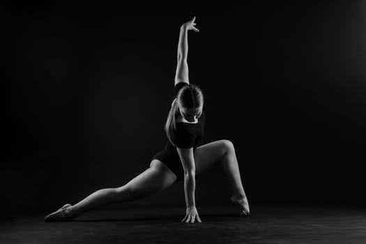 A girl gymnast in a swimsuit does tricks on white and dark background. Front view