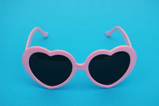 Pink heart-shaped sunglasses on a blue background...Fashionable glamorous women's glasses.