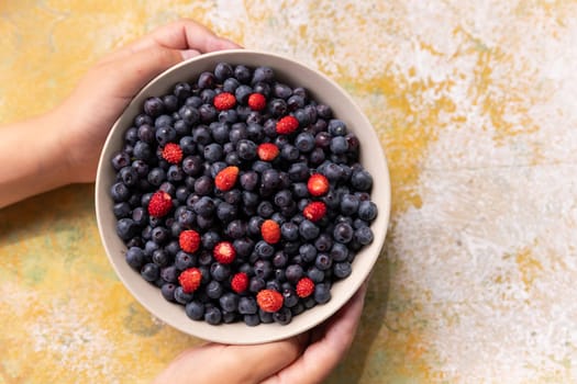 Strawberries and blueberries arranged in a heart shaped bowl on a rustic wooden table.