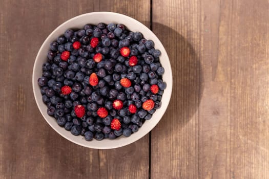 Strawberries and blueberries arranged in a heart shaped bowl on a rustic wooden table.