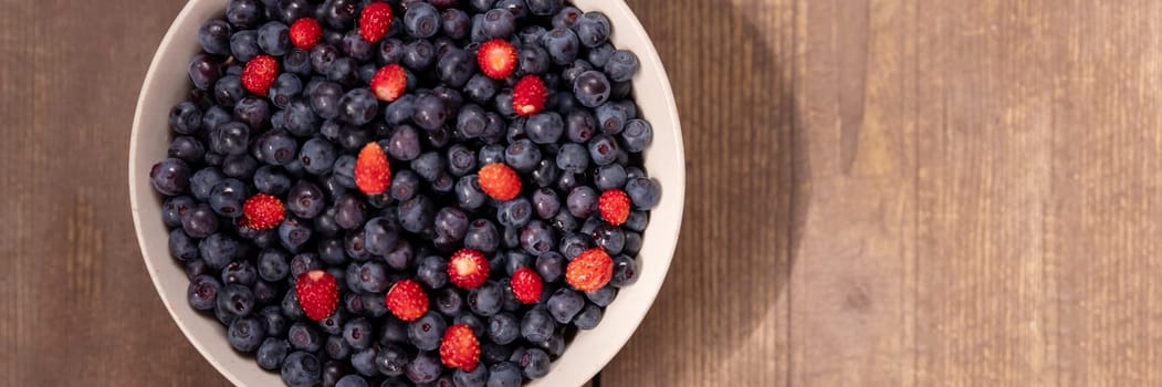 Strawberries and blueberries arranged in a heart shaped bowl on a rustic wooden table.