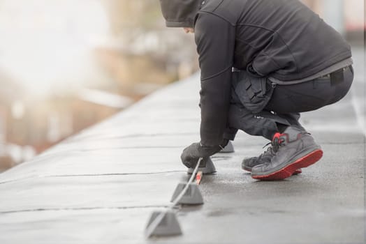 Ground wire. A worker lays a ground cable on the roof of a building. Electrician fixing aluminum wire for grounding solar panels.