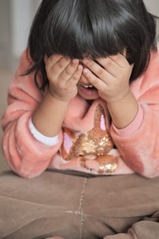 a upset child girl cover her face with hand .