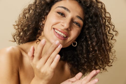 Woman beauty face close-up applying anti-aging moisturizer with fingers of her hand, skin health nails and hair, hair dryer style curly afro hair, body and beauty care concept. High quality photo