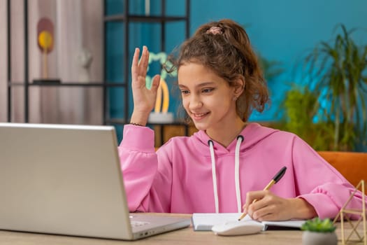 Preteen school girl using laptop for online lesson, doing homework, makes notes in notebook, answers question asked by teacher. Distance learning education. Child, kid at home. Video call by webcam
