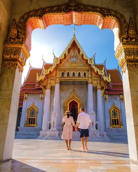 A couple of men and women visit Wat Benchamabophit temple in Bangkok Thailand, The Marble temple in Bangkok. Asian woman with a hat and European men visiting a temple in Bangkok