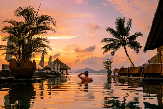 Luxury swimming pool in a tropical resort, relaxing holidays in Seychelles islands. La Digue, Young man during sunset by swim pool Seychelles