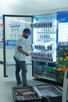 Jakarta, Indonesia. April 20, 2023. A young man is refilling the items on the vending machine at MRT Station. Public service photography.