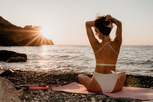 Young woman in swimsuit with long hair practicing stretching outdoors on yoga mat by the sea on a sunny day. Women's yoga fitness pilates routine. Healthy lifestyle, harmony and meditation concept.