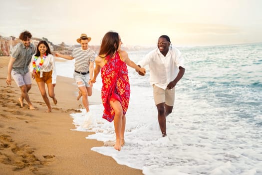 Young multiracial happy, smiling group of friends running along seaside during vacation travel. Holiday concept.
