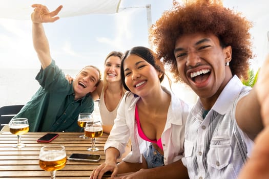 African American young man taking selfie with multiracial friends at a beach bar celebrating summer together with beer. Lifestyle and summertime concept.
