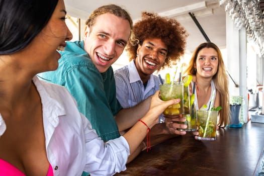 Hispanic young woman and multiracial friends toasting with mojito cocktails at a beach bar. Vacation concept.