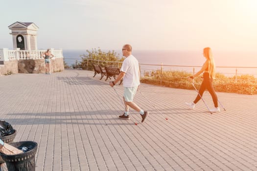 Happy Middle aged couple or friends practicing nordic walking in park near sea. Mature couple with trekking poles walking, practicing Nordic walking outdoors. Aging youthfully and sport concept.