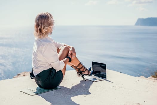 Happy girl doing yoga with laptop working at the beach. beautiful and calm business woman sitting with a laptop in a summer cafe in the lotus position meditating and relaxing. freelance girl remote work beach paradise