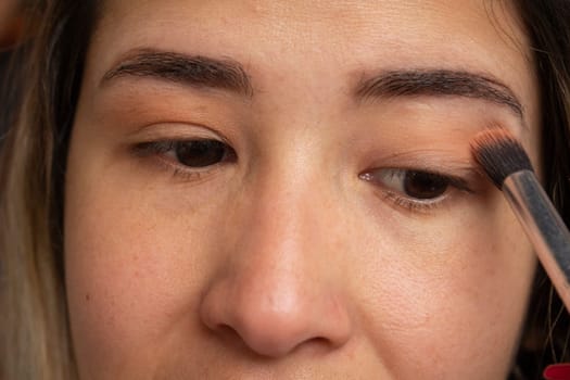 Caucasian woman looking in the mirror while putting on her eye makeup. High quality photo