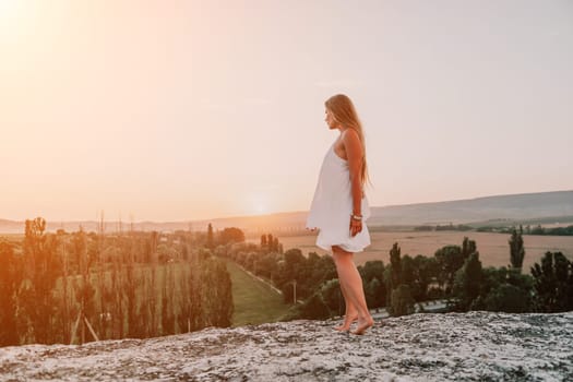 Romantic beautiful bride in white dress posing with sea and mountains in background. Stylish bride standing back on beautiful landscape of sea and mountains on sunset