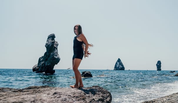 Woman travel sea. Young Happy woman in a long red dress posing on a beach near the sea on background of volcanic rocks, like in Iceland, sharing travel adventure journey