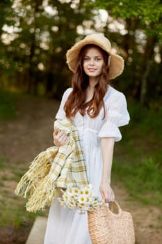 portrait of a cute woman in a wicker hat, light dress and with a plaid in her hands resting in nature. High quality photo