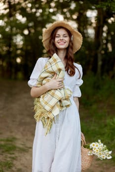 a happy, romantic woman stands in a light dress with a hat on her head and a plaid in her hands in the park. High quality photo