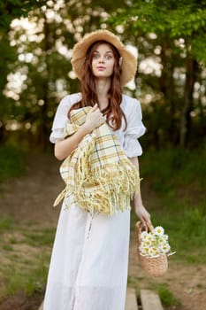 portrait of a cute woman in a wicker hat, light dress and with a plaid in her hands resting in nature. High quality photo