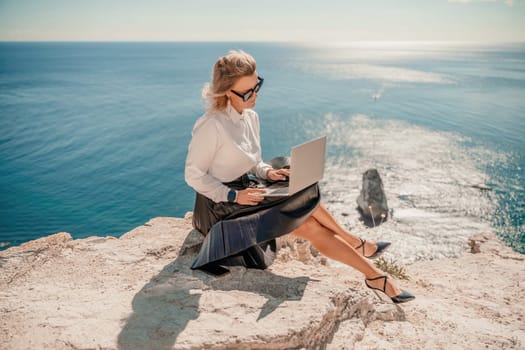 Business woman on nature in white shirt and black skirt. She works with an iPad in the open air with a beautiful view of the sea. The concept of remote work