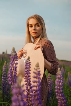 A beautiful woman in a straw hat walks in a field with purple flowers. A walk in nature in the lupin field.