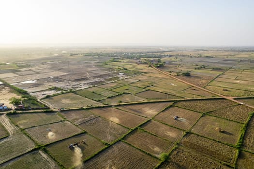 drone shot of tractor winnowing grain in many square farms feilds with six lane delhi, jaipur, surat, baroda, ahmedabad and mumbai highway in India