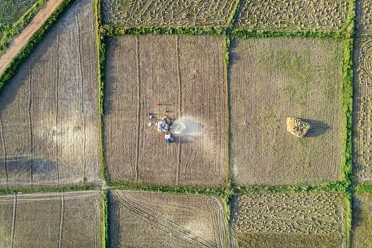 straight down aerial drone shot showing square small farms with tractor in between winnowing grain during the harvest season near Rajasthan India