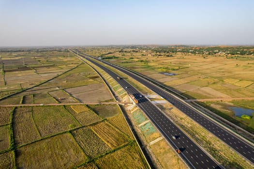 locked tripod aerial drone shot of new delhi mumbai jaipur express elevated highway showing six lane road with green feilds with rectangular farms on the sides