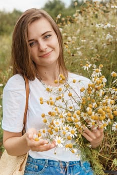 Beautiful young woman in nature with a bouquet of daisies. Field daisies, field of flowers. Summer tender photo.