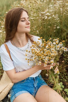 Beautiful young woman in nature with a bouquet of daisies. Field daisies, field of flowers. Summer tender photo.