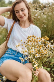 Beautiful young woman in nature with a bouquet of daisies. Field daisies, field of flowers. Summer tender photo.