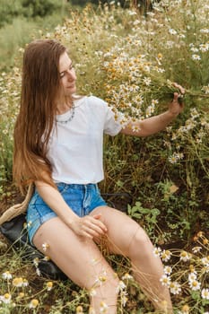 Beautiful young woman in nature with a bouquet of daisies. Field daisies, field of flowers. Summer tender photo.